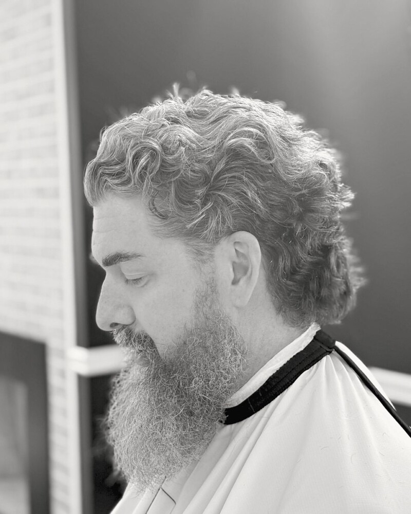 Silver curly hair shaped with a full beard, in profile