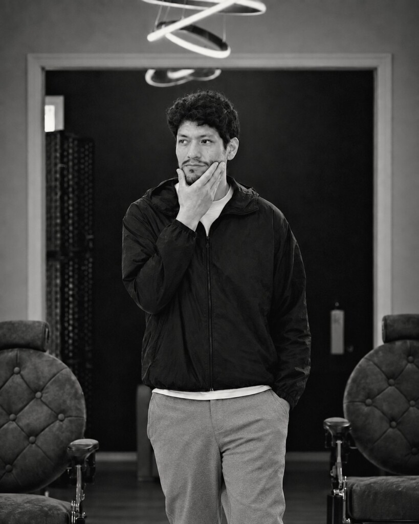 Josue Alegria, hand on his chin, standing between two tufted barber chairs under VQ’s ring lights